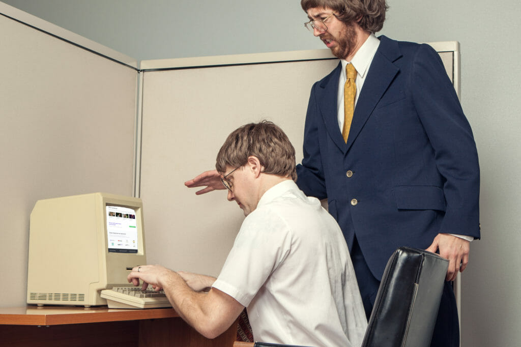 Two men working in front of a vintage computer. 1980s.